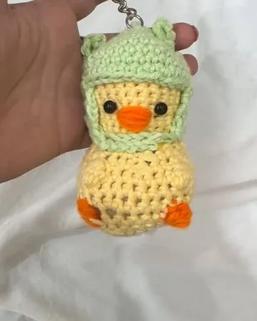 Crochet duckling keychain wearing a green frog hat