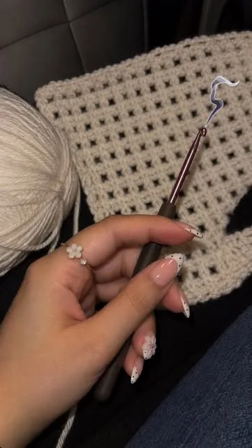 Hands holding a crochet hook over a cream mesh piece and a ball of yarn