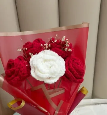 Crochet bouquet of red roses around one white rose in red wrap